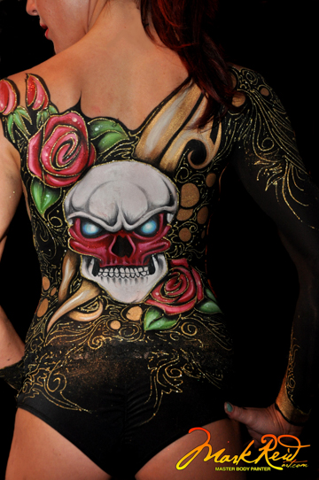 woman painted with an intricate painting of pink flowers leaves and a skull on her back and buttocks 